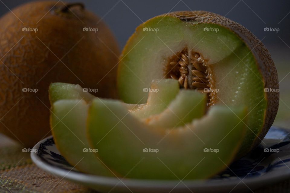 A  whole melon, a half of a melon and slides of melon on a plate.