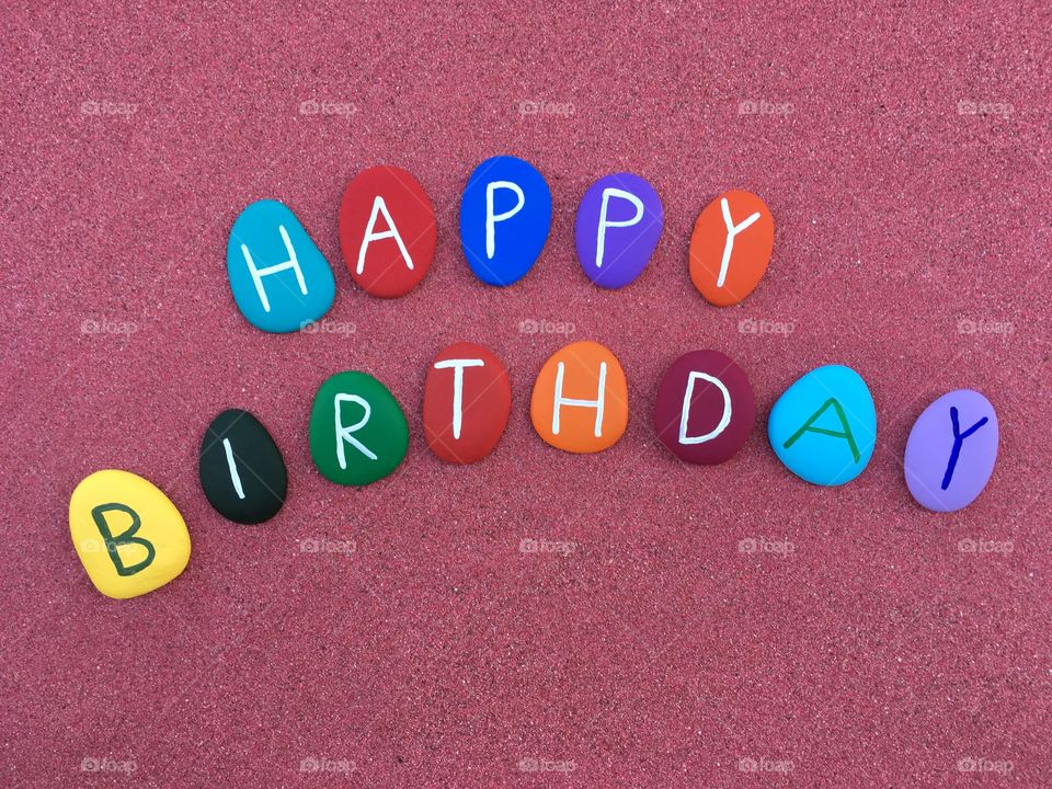 Happy Birthday on colored stone letters over red sand 