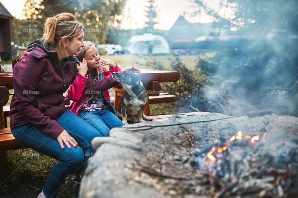 Family with dog sitting at campfire during summer vacation. Mother and daughter spending time on summer weekend. Vacation trip close to nature