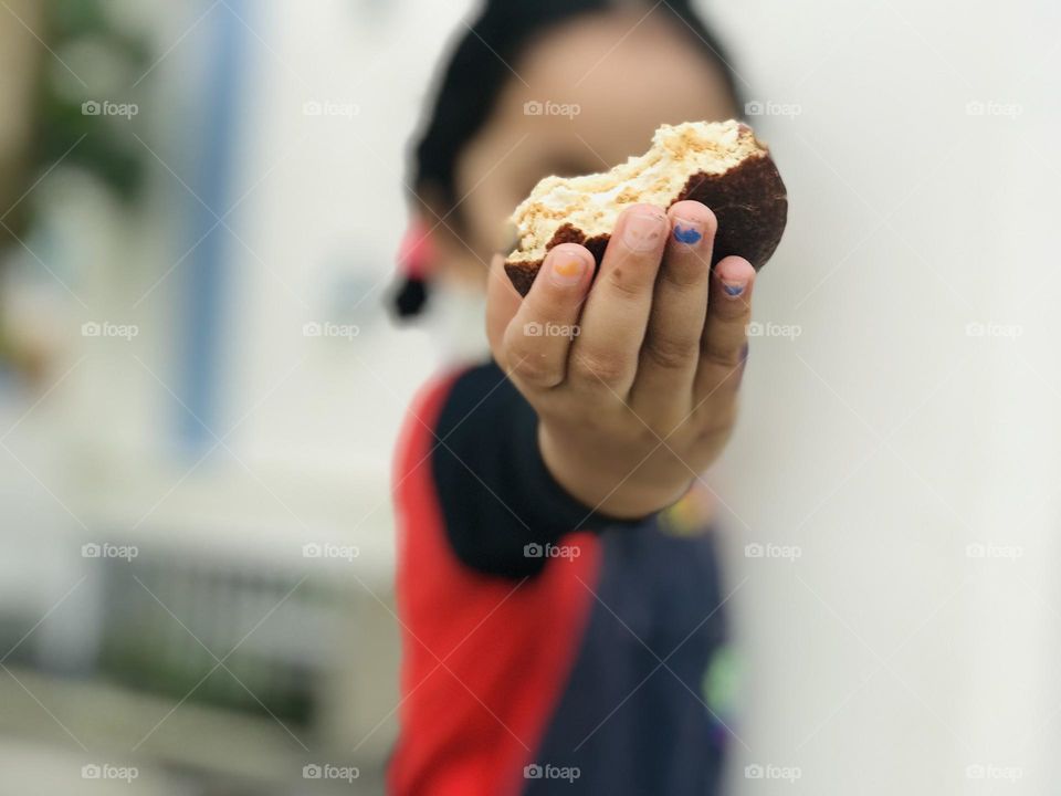 Baby girl holding half bite cookie in her hand and showing towards the camera 