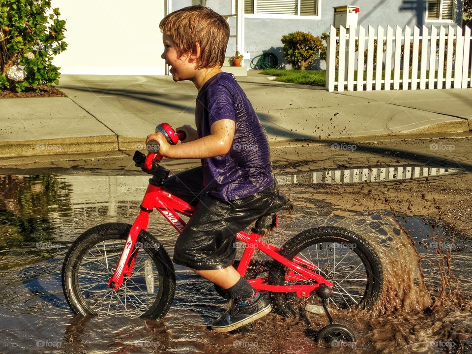 Joyful Young Boy Riding Bike Through Mud Puddle