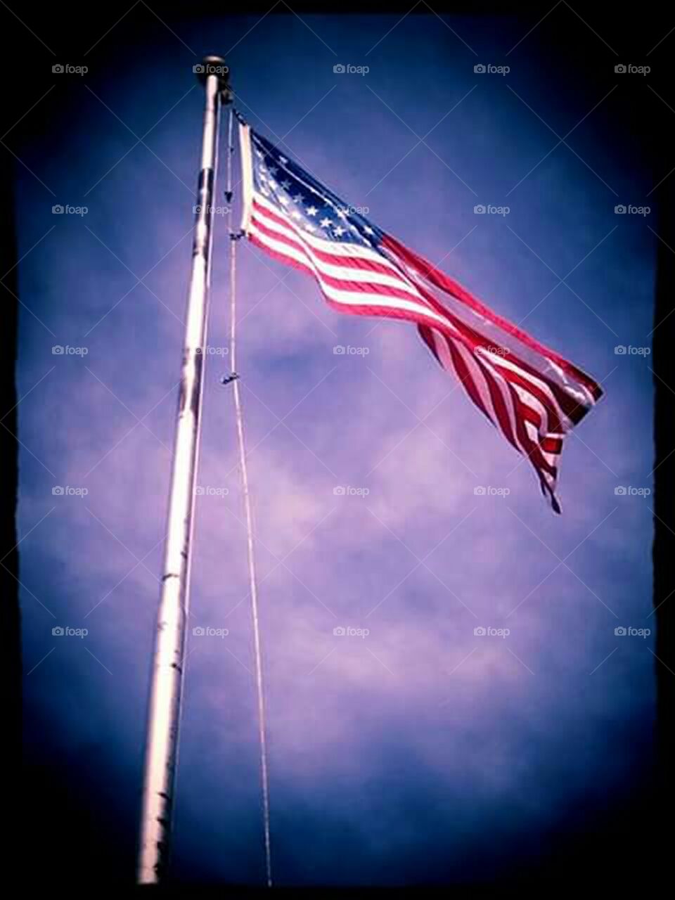 image of American flag on flag pole flying in the wind with blue sky background