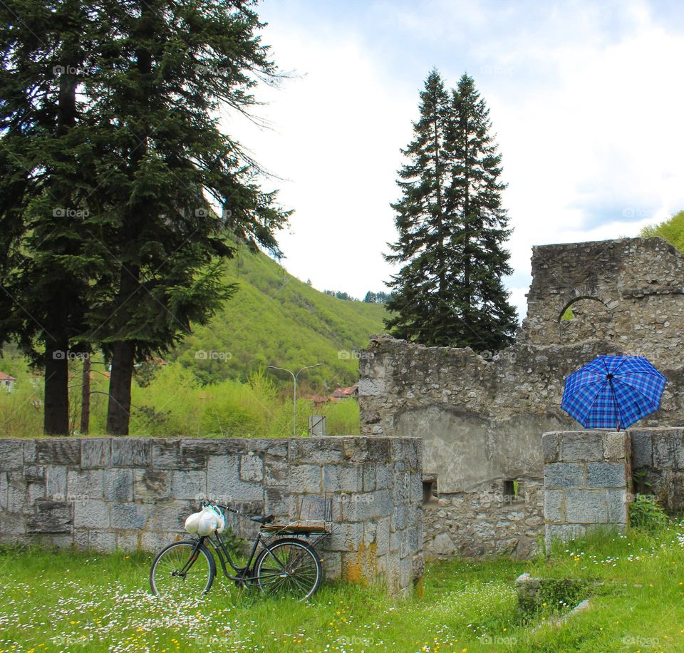 One lonely bicycle in nature leaning against the wall of a ruin and blue umbrella