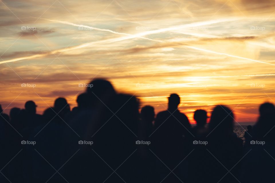 People standing on beach during sunset with giant 'X' in the sky written with clouds. . Silhouette of crowd standing watching sunset