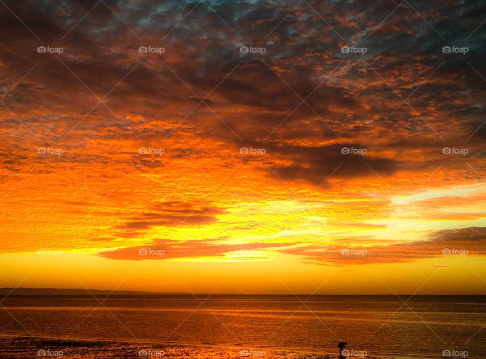 Silhouette person walking on the beach toward a spectacular sunrise on the ocean 