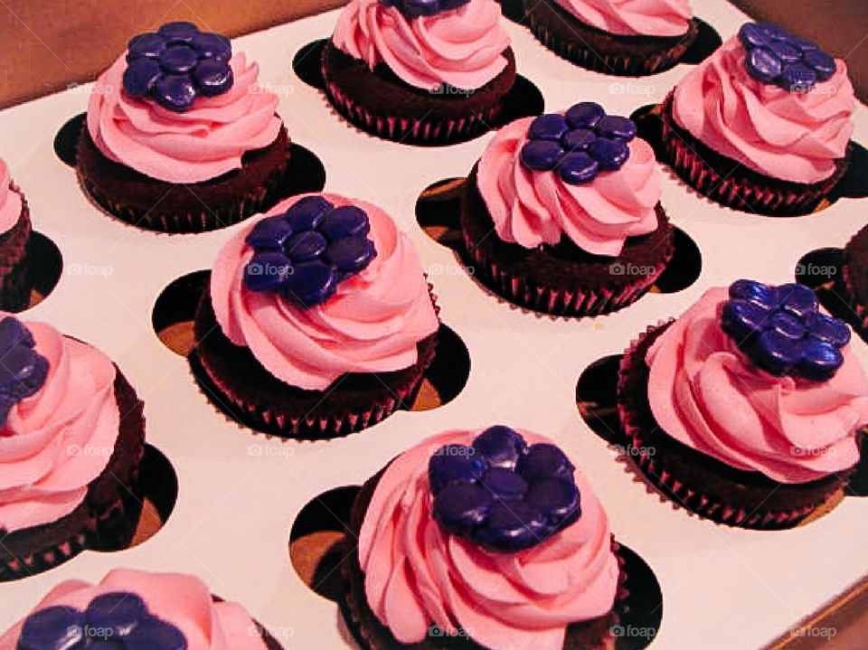 Chocolate cupcakes with pink icing with a purple fondant flower on top. 