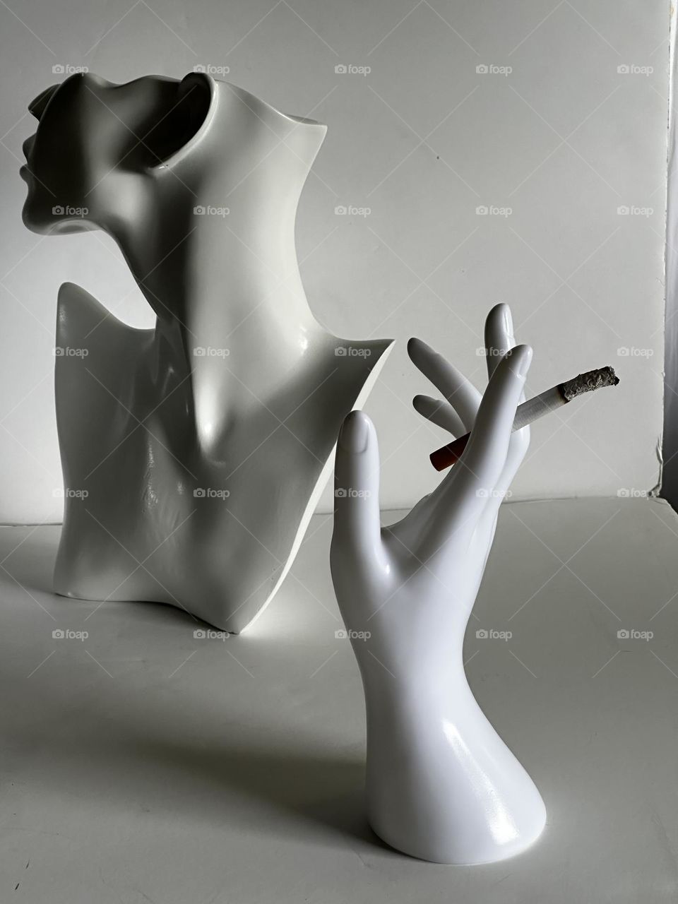 IPhone14 Pro shot of whtie mannequin jewelry bust with white mannequin hand holding lit cigarette on foam core background for Foap Disgust Mission