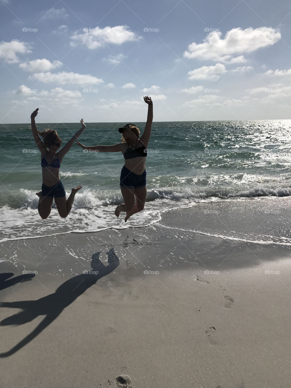 Two girls enjoying the sunny beach together jumping in the air 