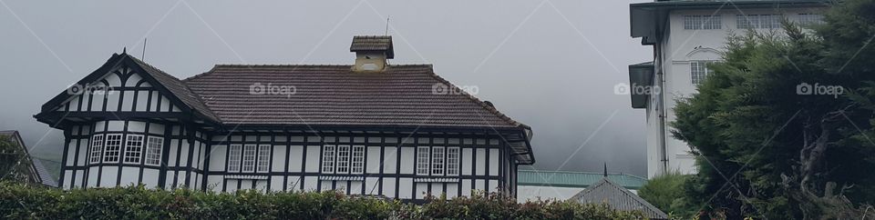 This is a photograph of a cottage surrounded by morning mist. It gives an image of an ancient cottage/ a bunglow.