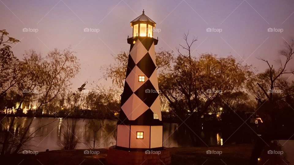 Lake Shore Lighthouse just before Night. Reflections of distant Shore Line, Distant Shore Lighting Reflective on Top of Lake Waters Captivating the Night.