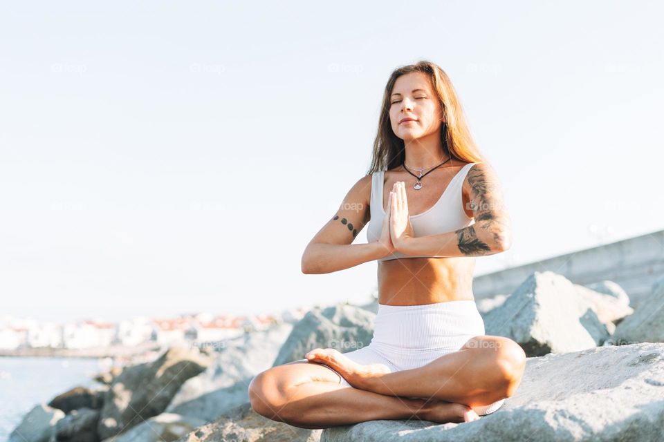Crop photo of young fit beautiful woman with long hair in white sport clothes practice yoga and enjoy life on the sea beach, mental and phisical health