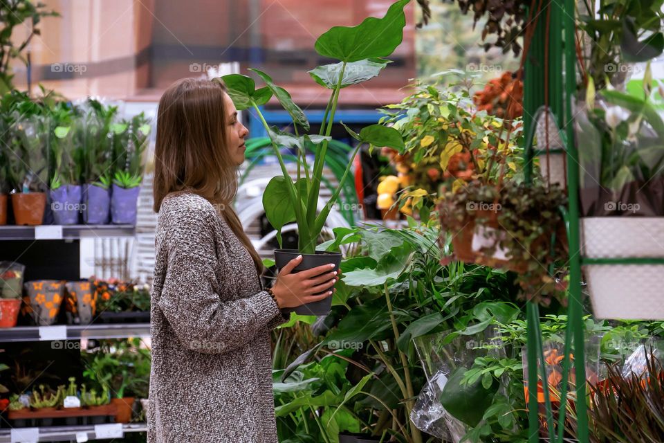 Young woman holding a pot with monstera in the middle of a flower store