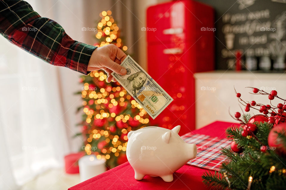 piggy bank with 100 dollars banknote in festive New Year atmosphere of scenery. Magical bokeh with Christmas tree and bright lights.