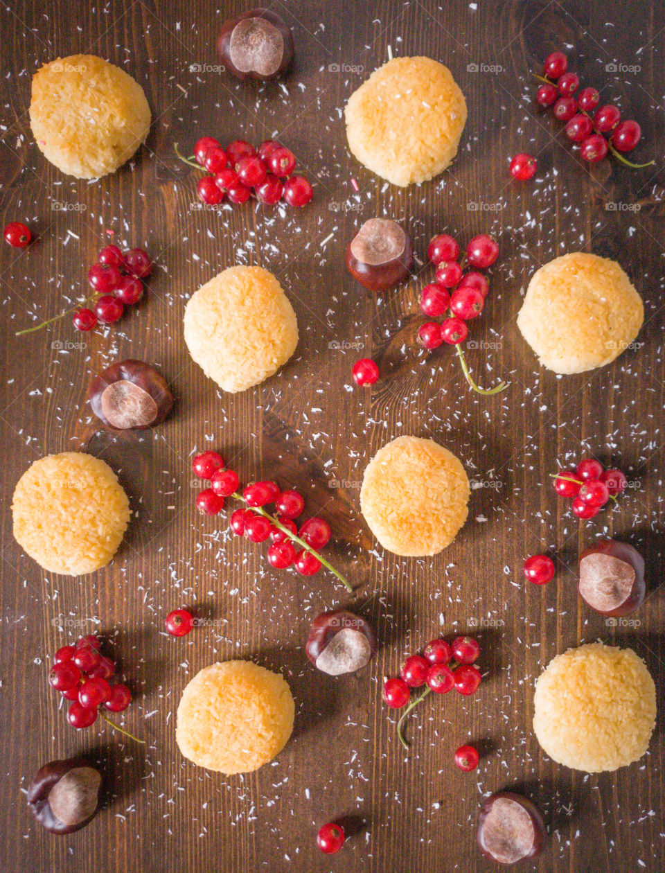 Food photography, top view. Coconut cookies with sprigs of red currant and peeled chestnuts sprinkled with coconut flakes on a wooden dark brown background. Autumn composition