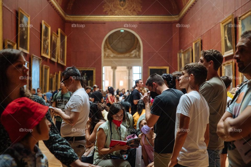 Different people and the amazing Louvre museum from Paris, enjoying the art, escaping from the heat, during summer holiday.