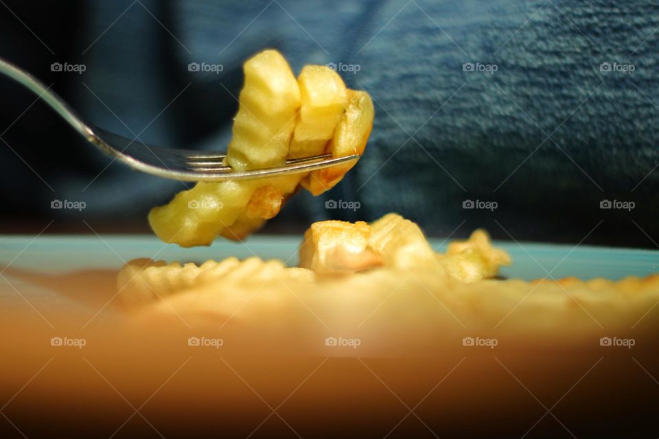 A blue plate with french fries and above it a fork with skewered french fries