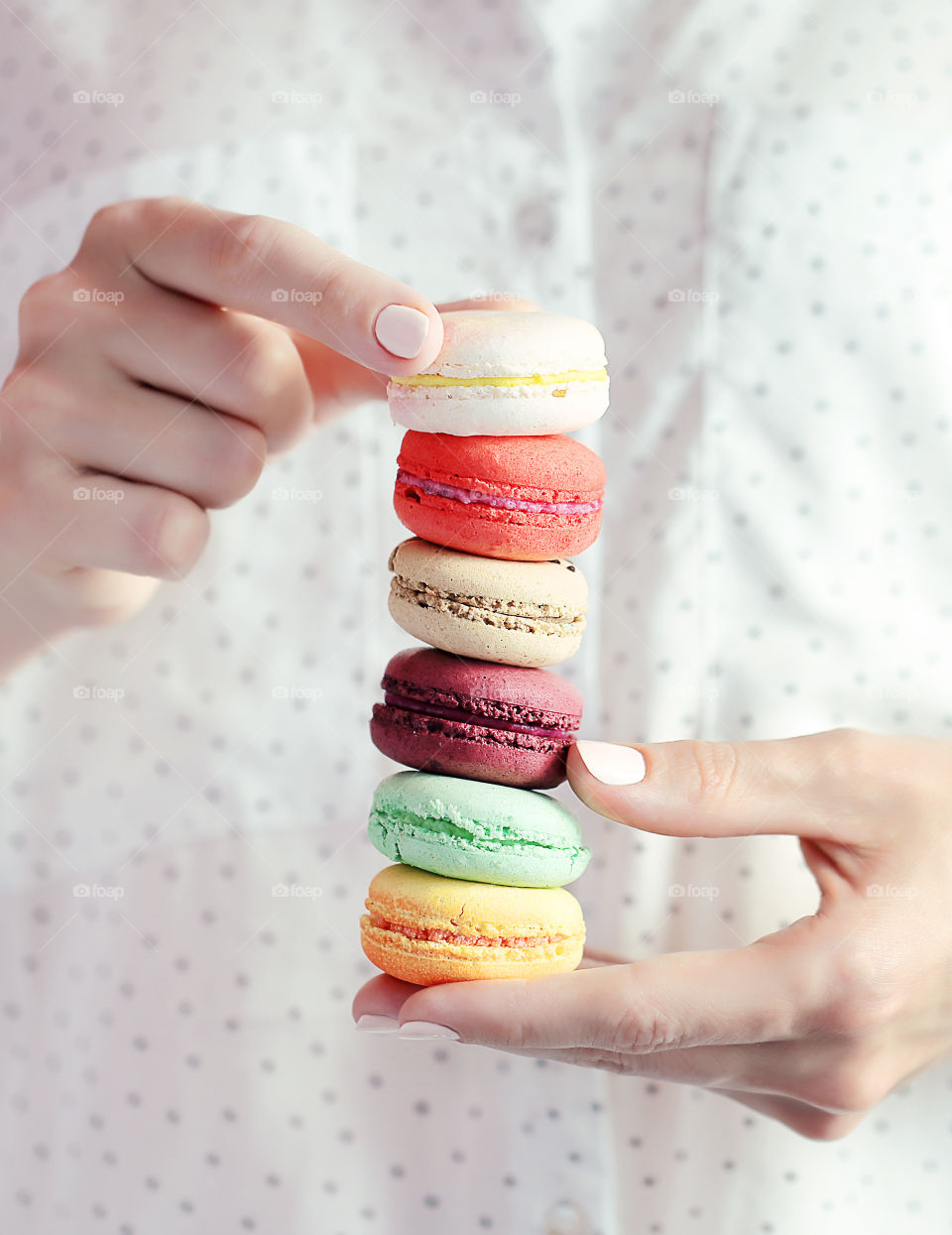 Tower of 5 colored macaron in the woman hands on the background of the polka dots shirt
