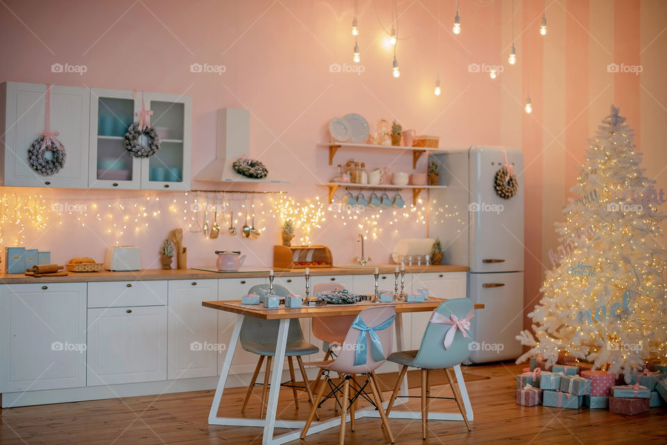 Festive winter cozy kitchen interior with garlands, decorations and gifts.  Christmas dinner at the decorated table.