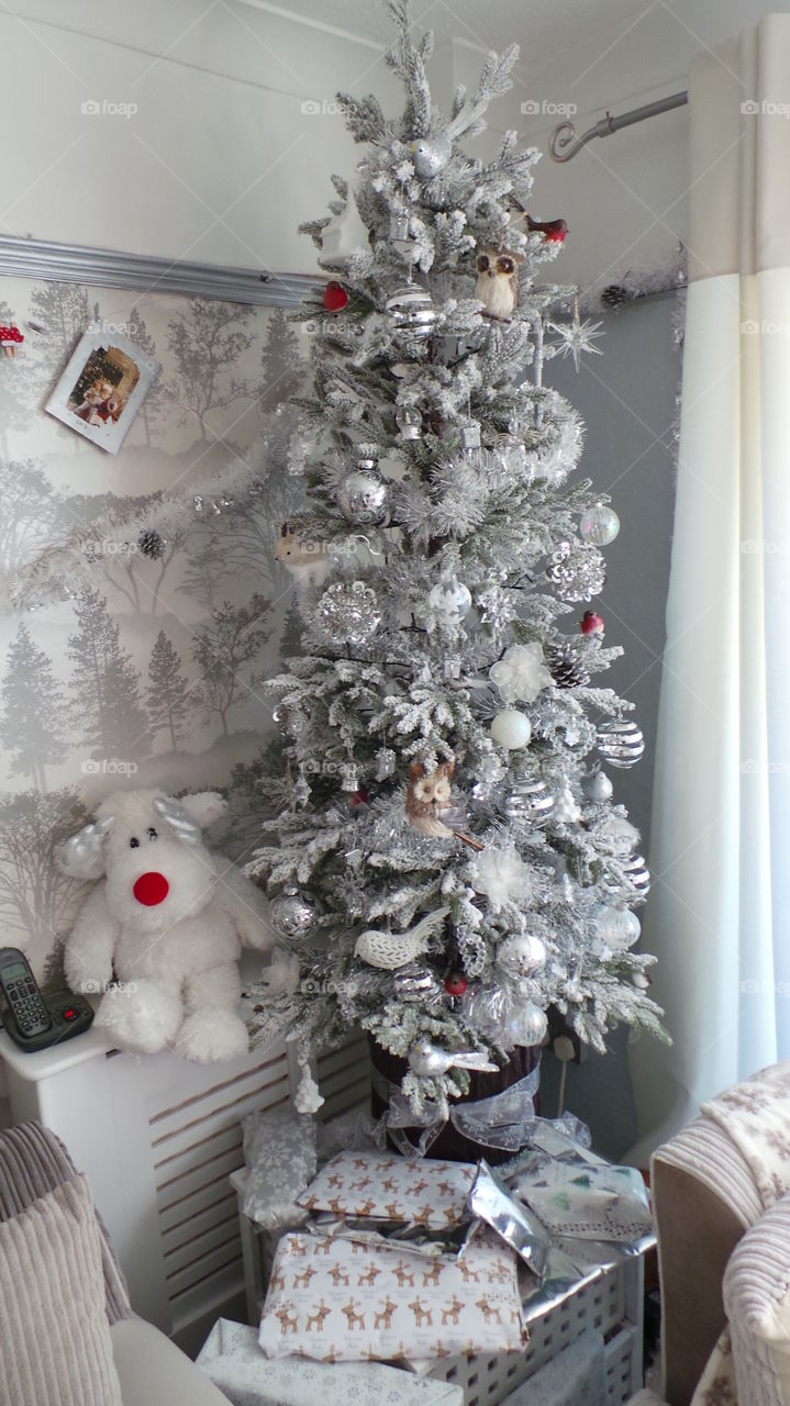 white and sliver decorated snowy Christmas tree. reindeer soft toy. gifts.