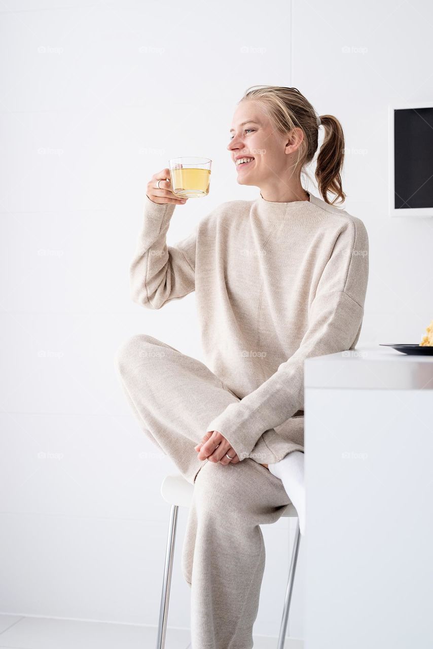 young woman in home comfy clothes drinking green tea in the kitchen