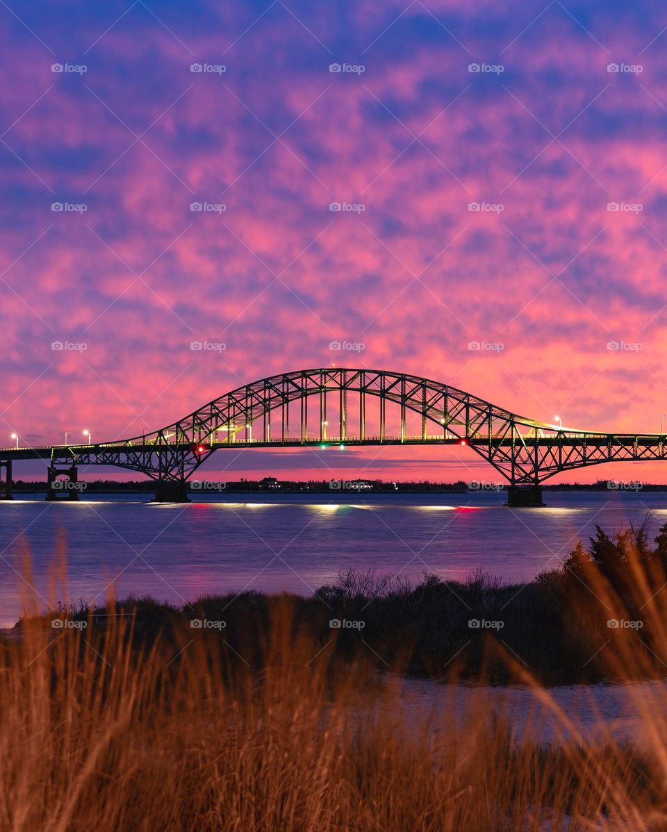 Vibrant colorful clouds over a long steel tied arch bridge with golden light from the street lamps reflecting in the water