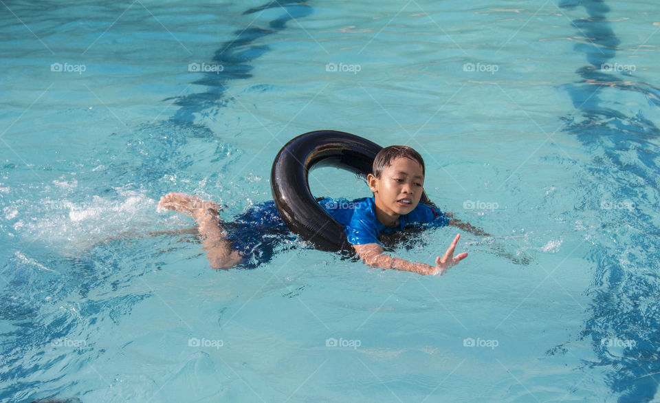 anak kecil yang sedang bermain di kolam renang dengan menggunakan pelampung ban berwarna hitam.