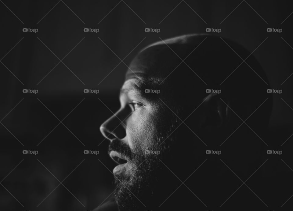 Black and white portrait of a bearded man and his profile with stark contrast and dark shadows. 