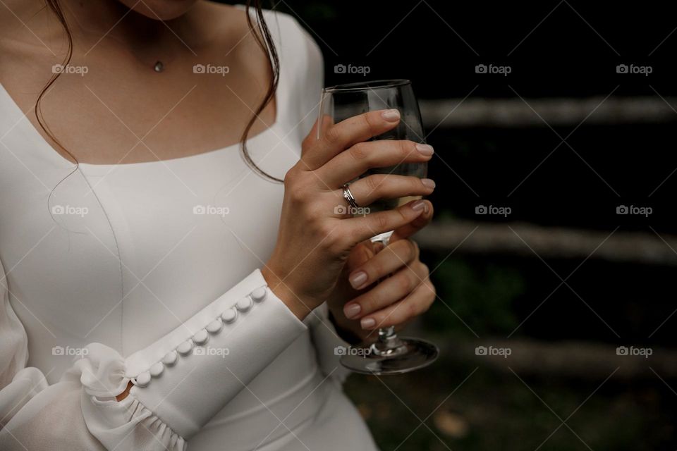 Bride in white wedding dress with nude manicure hold glass of champagne