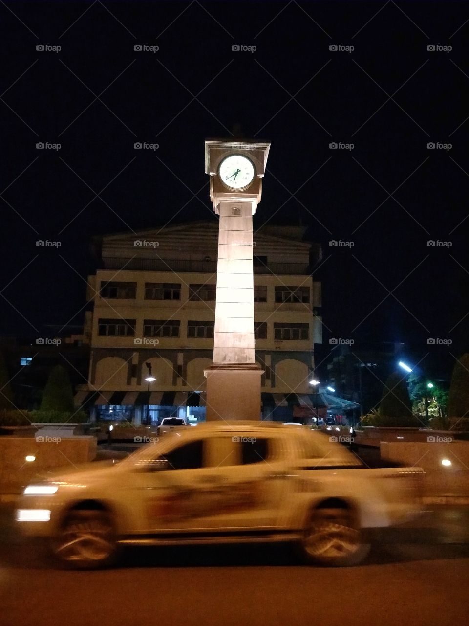 The car is running in front of the clock tower.