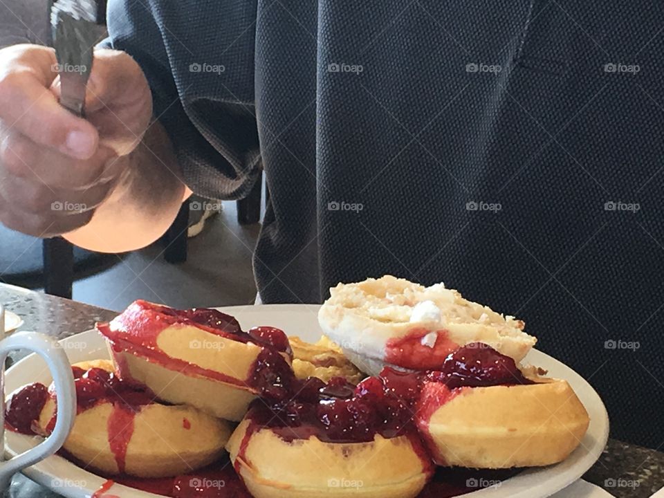 A man sitting down at a table eating a large plateful of delicious round waffles topped with strawberries and whipped cream