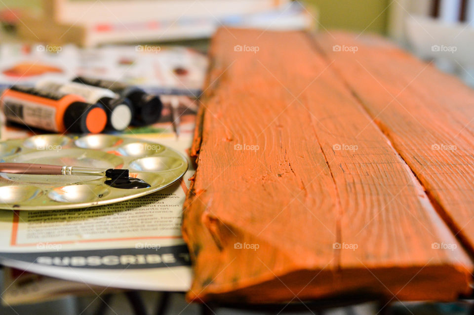 Piece of wood painted orange beside a paint pallet and paint brush