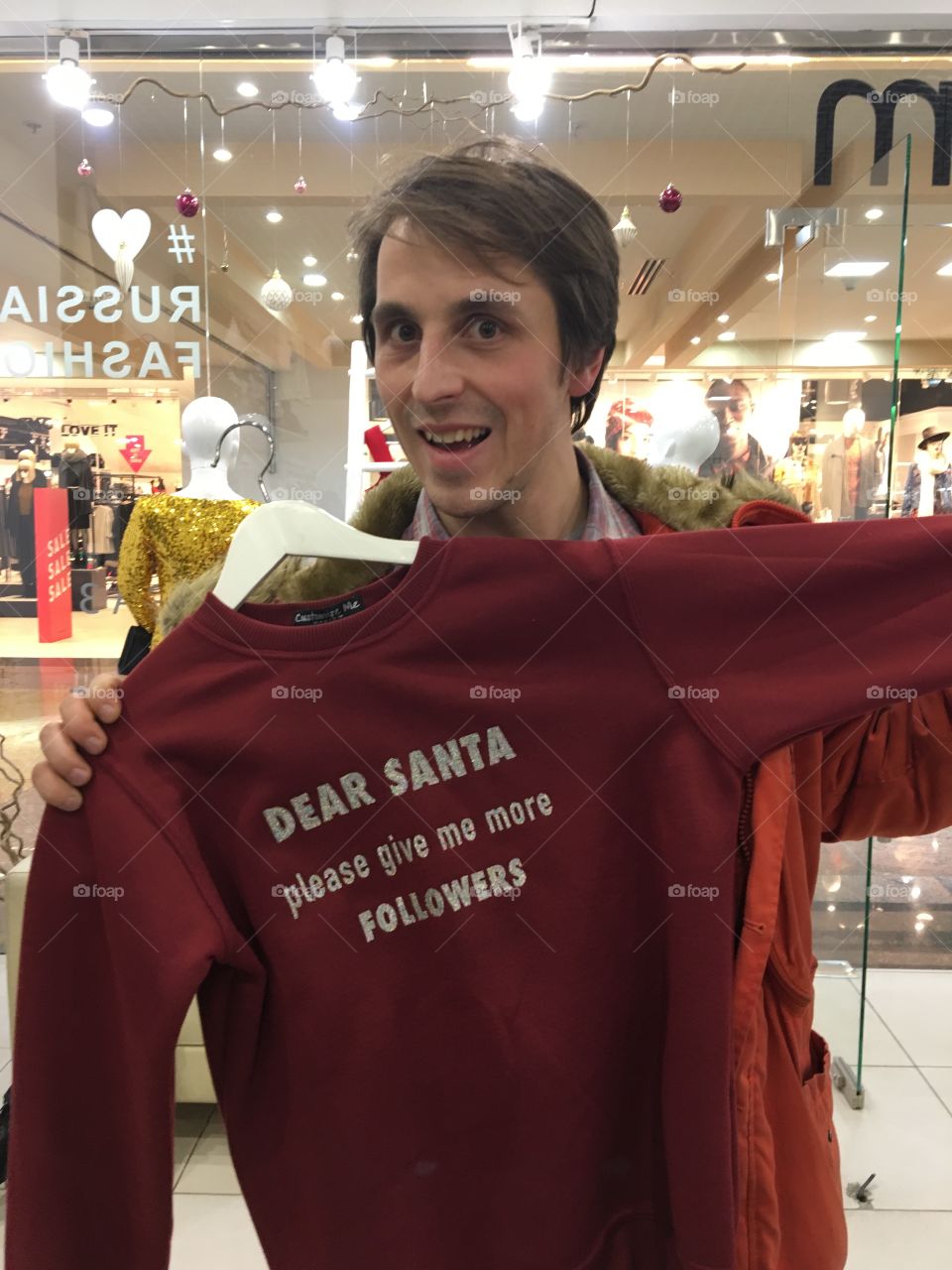 Man in store smiling and trying sweatshirt with words about more likes and followers for christmas 