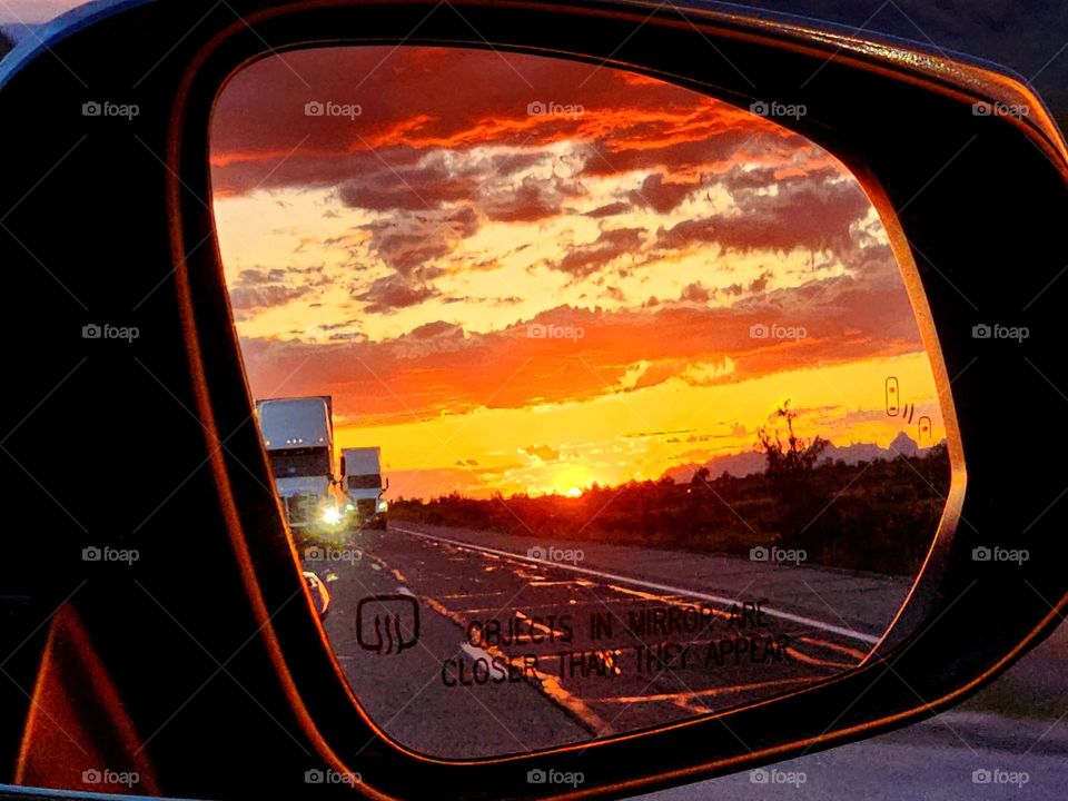 The setting sun fills a vehicle's side mirror with a beautiful sight as the car heads eastbound through the Arizona desert