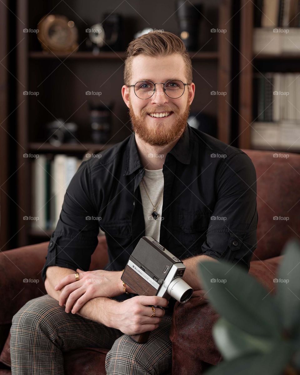 Young man seating in a chair for a portrait, camera in hand