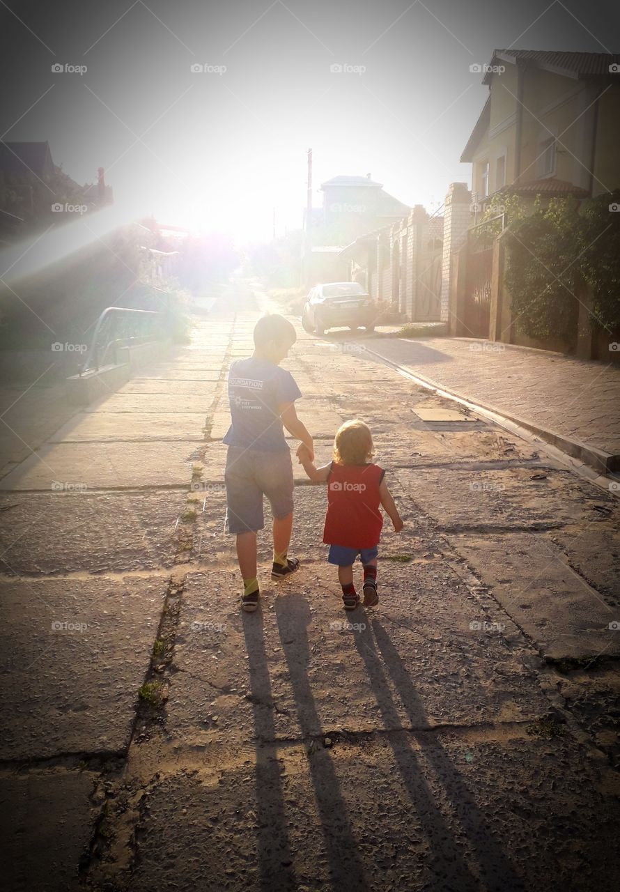 two boys are walking alone the road in the rays of sunset