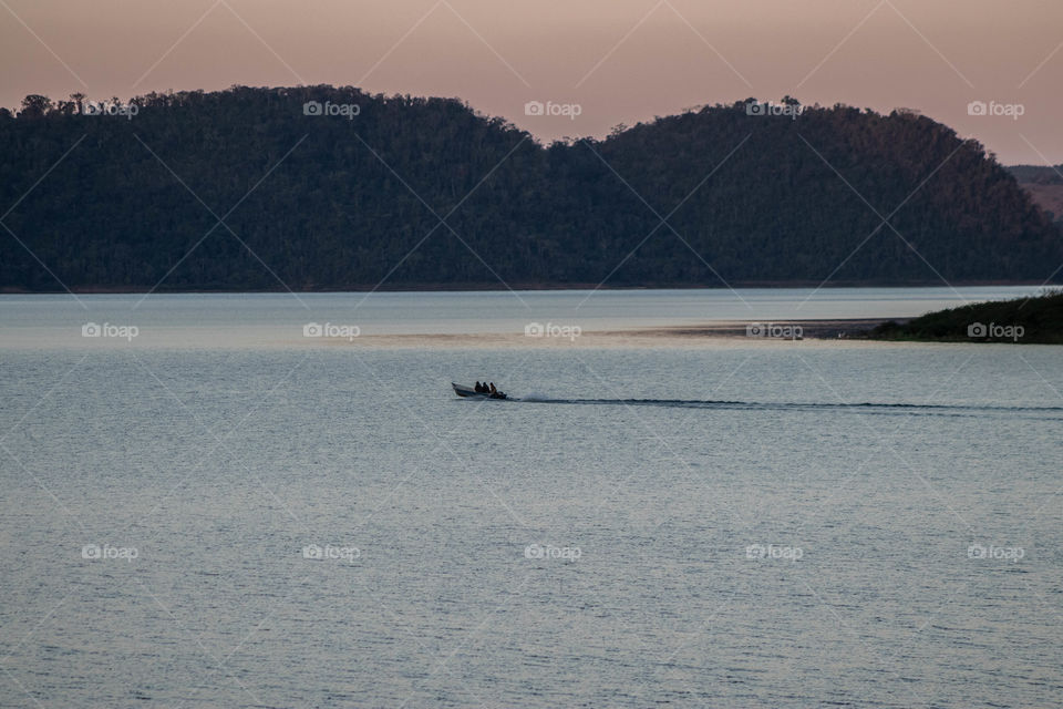 Barco atravessando represa em por do sol bonito.