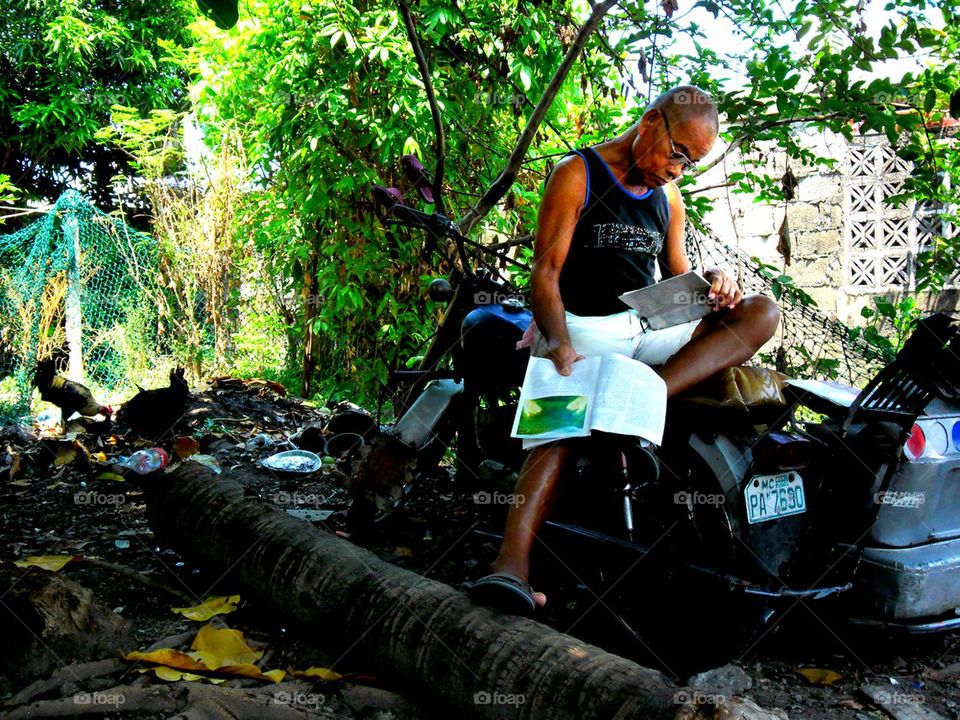 asian man reading magazines under the shade of a tree