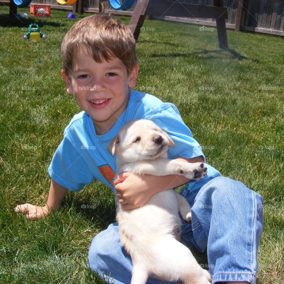 Young boy sitting in the grass holding a yellow lab puppy 