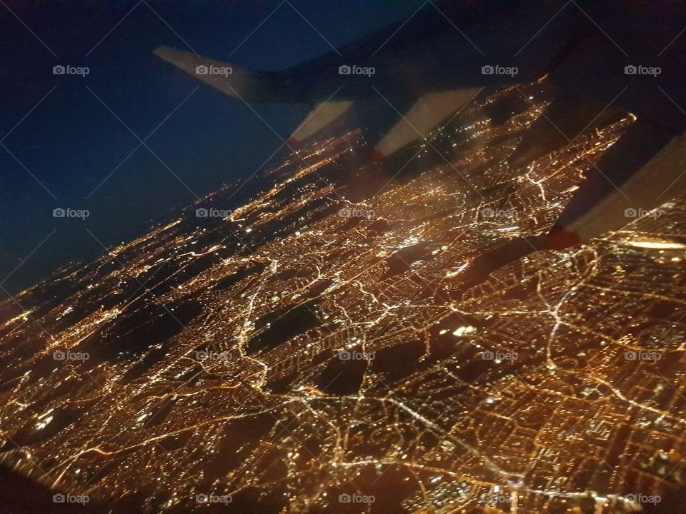 Airplane window view flying over illuminated glowing lights of cities and streets below