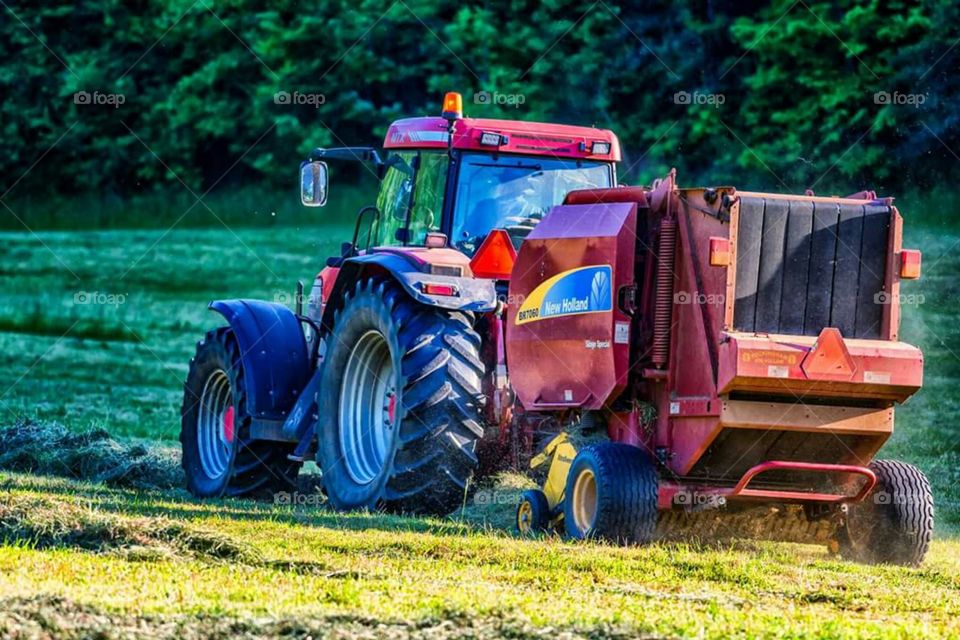 Red tractor and hay baler harvesting hay