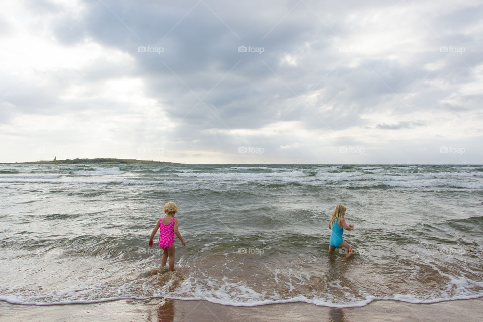 Twi sisters playing at the beach of Tylösand outside Halmstad in Sweden. It's about to get stormy weather but the girls is having fun swimming and playing in the water.