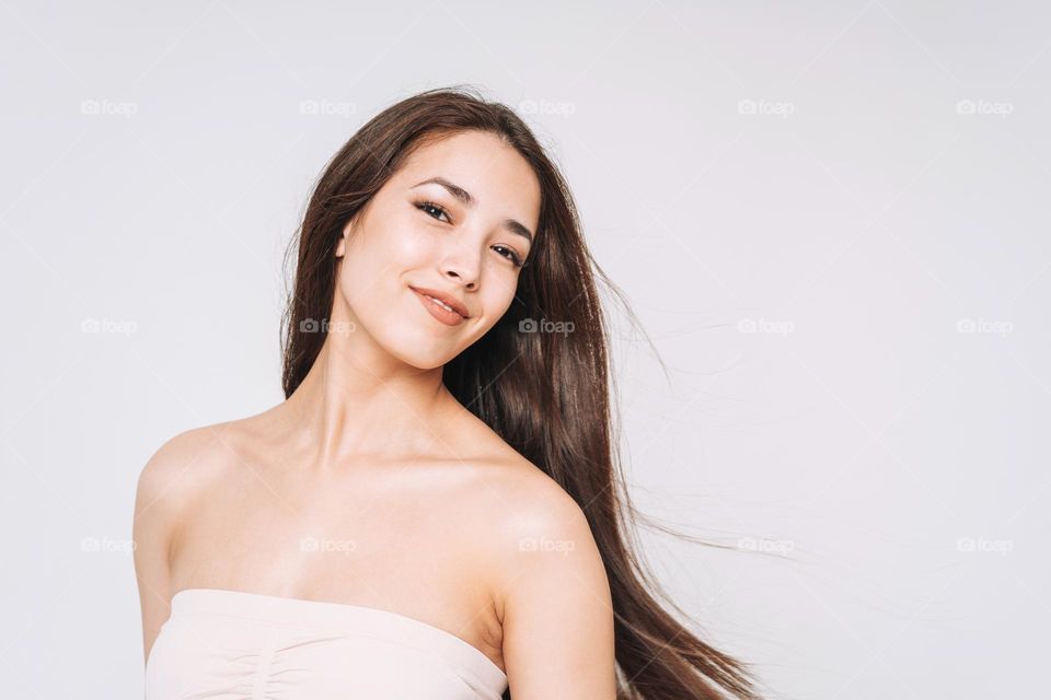 Beauty portrait of happy young beautiful asian woman with healthy dark long hair in top bando on white background isolated