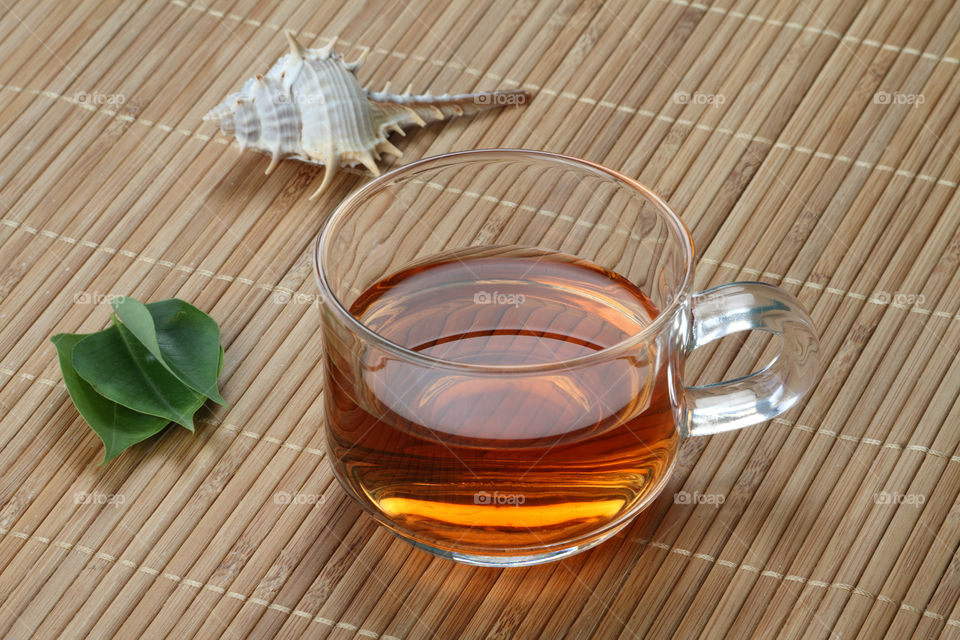 Tea cup with tea leaves and shell on wooden bamboo background