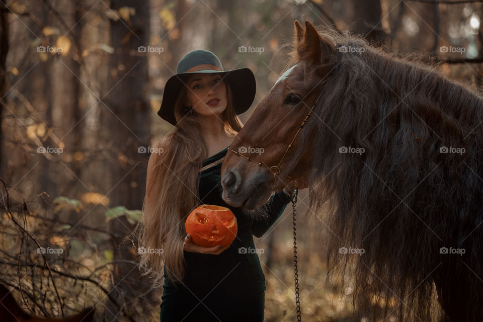 Woman in witch wear with horse in autumn park 