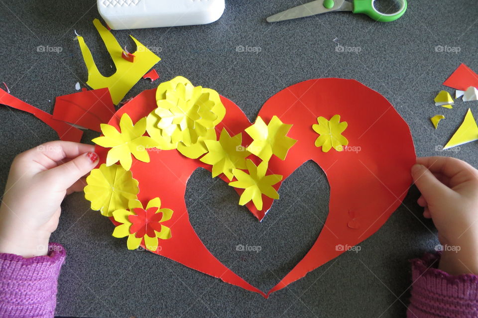 The four-year-old daughter made a gift for her mother: a red heart with yellow flowers is glued on a yellow cardboard. Perfect gift for mom. Happy Valentine's Day!