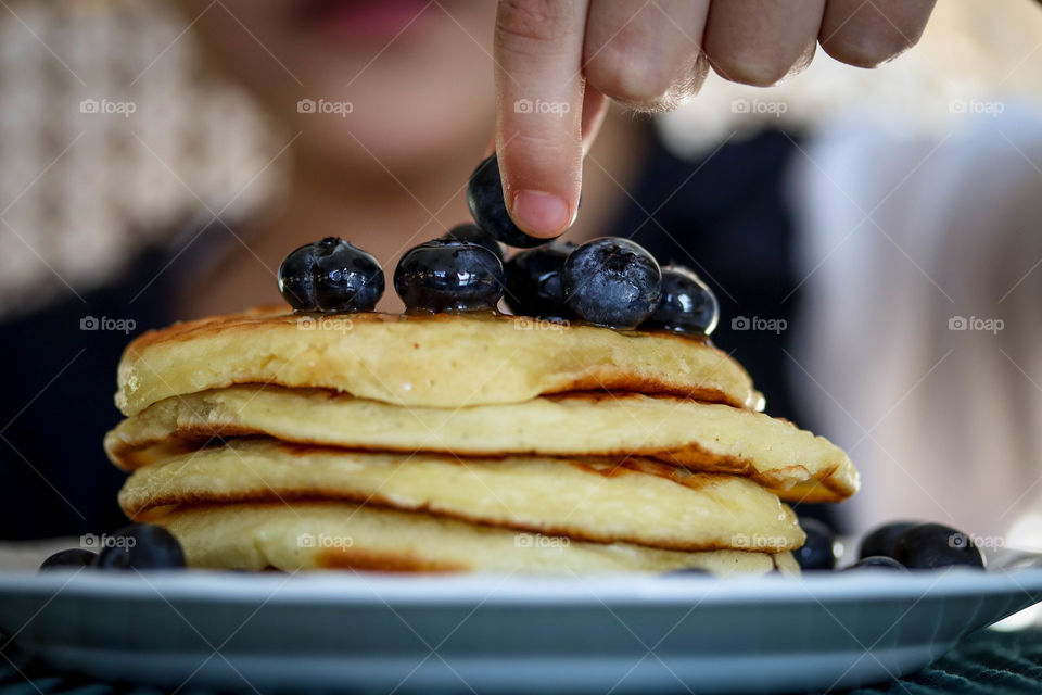 Child is eating pancakes with blueberries