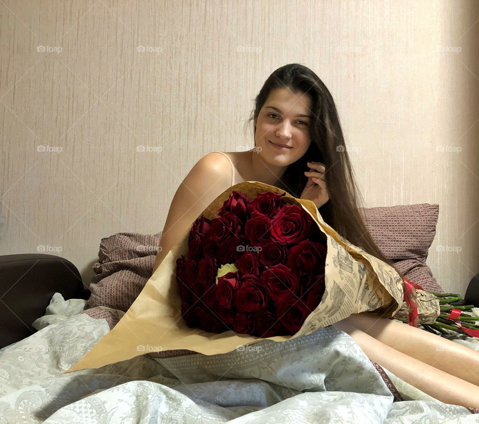 pretty girl sitting in bed with a huge bouquet of roses