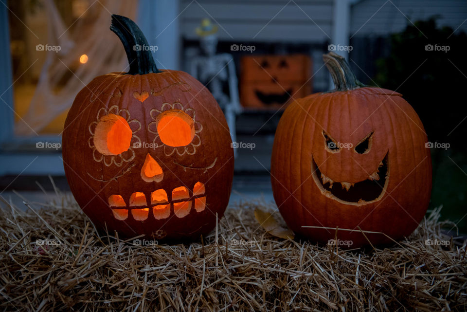 Close-up of two carved pumpkins outdoors on a front porch in the dark at night