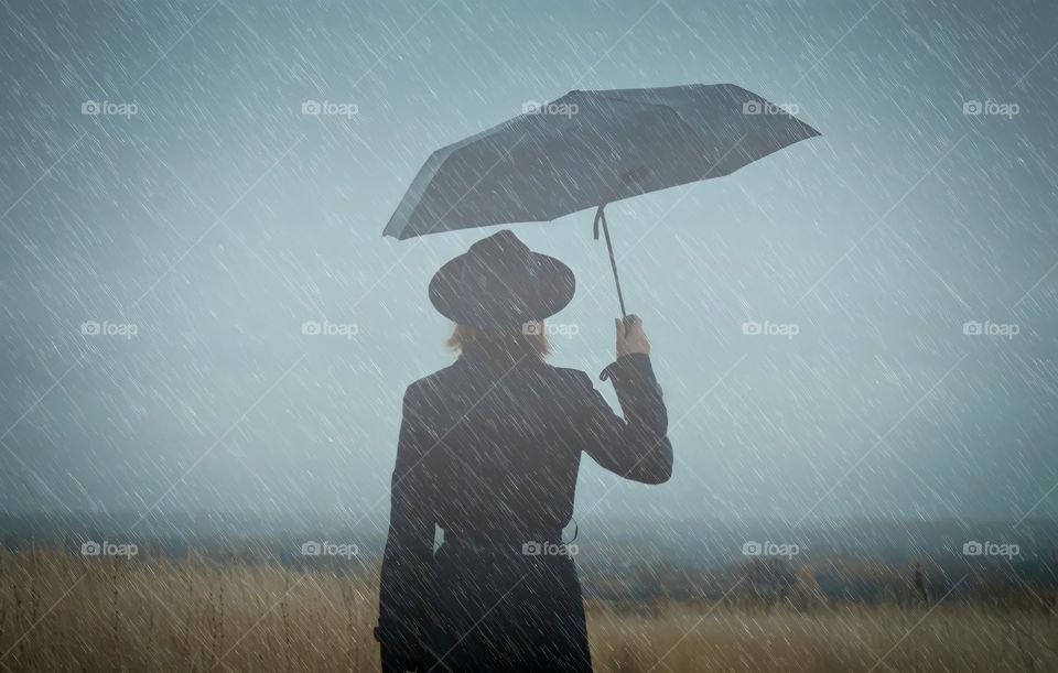 Woman Walking Alone in the Rain - Loneliness Concept.

Woman with umbrella in the rain watching the horizon.