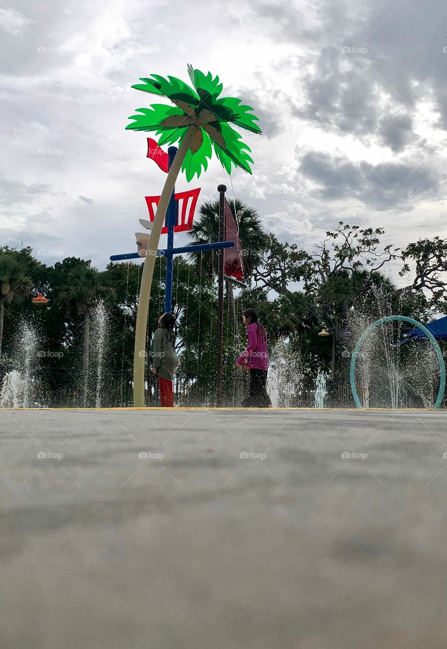 Children having lots of fun in the water at the colorful kids splash pad at the city park for children during a really warm day in Florida.